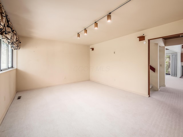 unfurnished room featuring stairway, baseboards, rail lighting, and light carpet