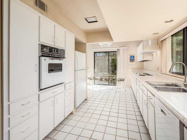 kitchen featuring wall chimney exhaust hood, white appliances, white cabinets, visible vents, and a sink