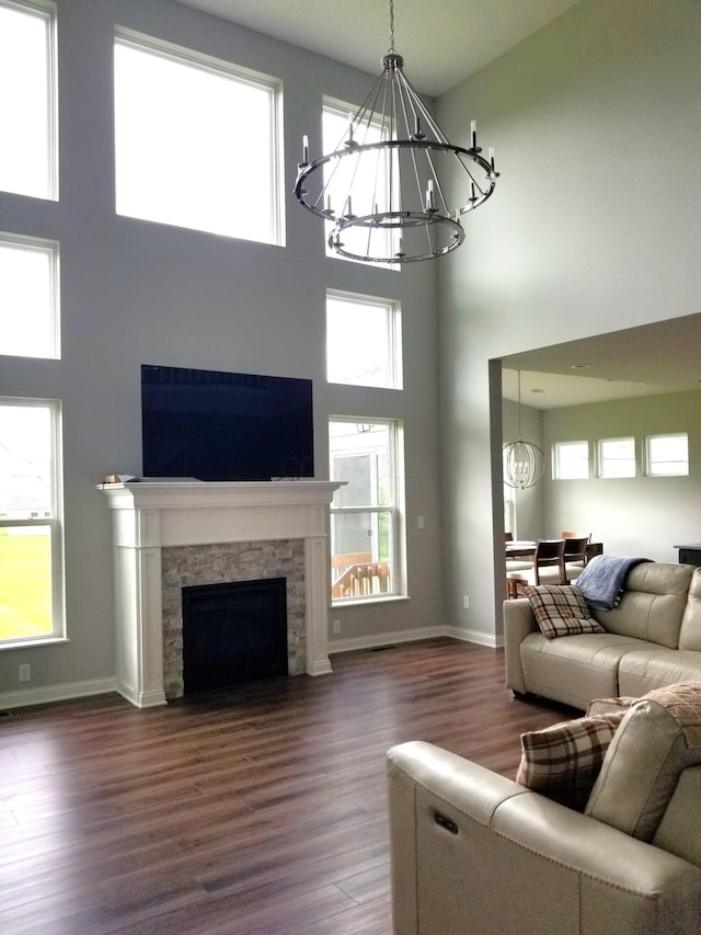 living room with a notable chandelier, baseboards, a stone fireplace, and dark wood finished floors