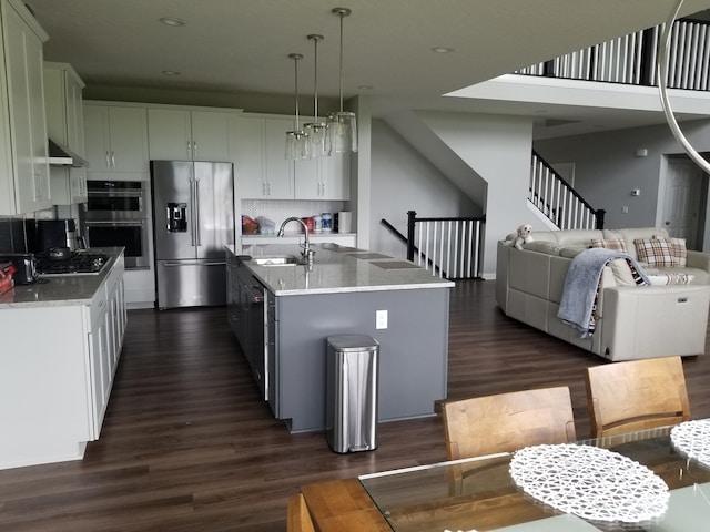kitchen with a sink, wall chimney exhaust hood, dark wood finished floors, open floor plan, and stainless steel appliances