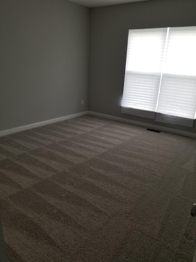 spare room featuring baseboards, dark carpet, and visible vents