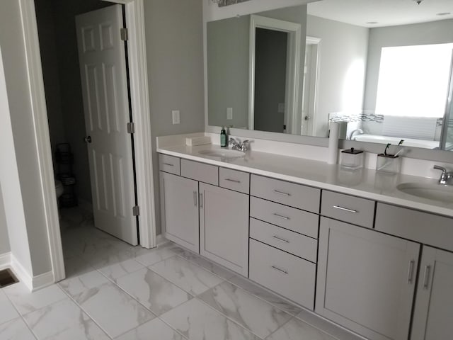 full bath featuring marble finish floor, a sink, toilet, and double vanity