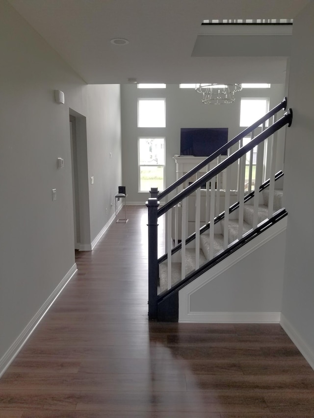 stairway with baseboards, wood finished floors, and an inviting chandelier
