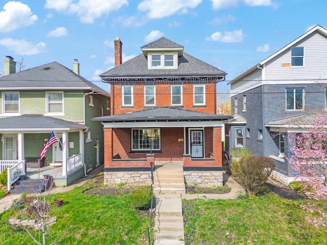 traditional style home with a front yard, brick siding, a porch, a shingled roof, and a chimney