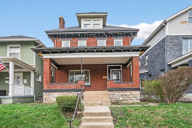 american foursquare style home featuring brick siding, a chimney, and covered porch