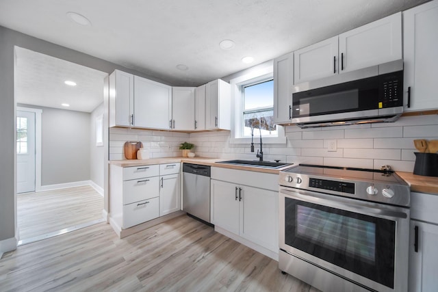 kitchen featuring a sink, white cabinetry, appliances with stainless steel finishes, light wood-style flooring, and decorative backsplash