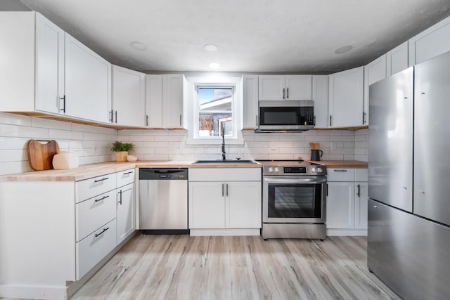 kitchen with a sink, tasteful backsplash, appliances with stainless steel finishes, light wood-style flooring, and white cabinets