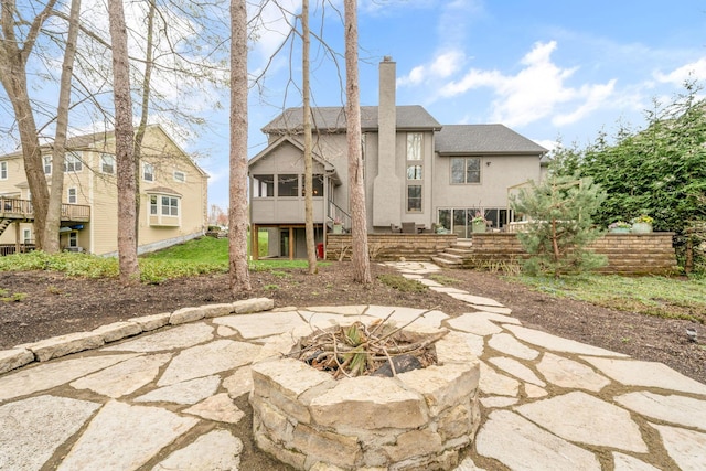 back of property with a sunroom, stucco siding, a fire pit, stairs, and a chimney