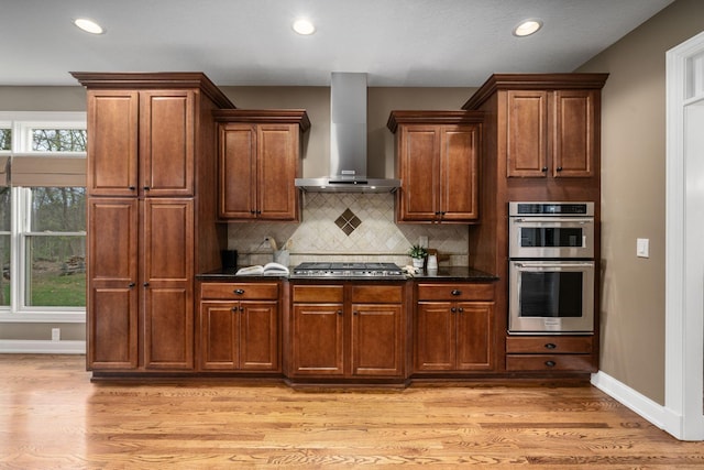 kitchen with wall chimney range hood, appliances with stainless steel finishes, plenty of natural light, and light wood-style floors