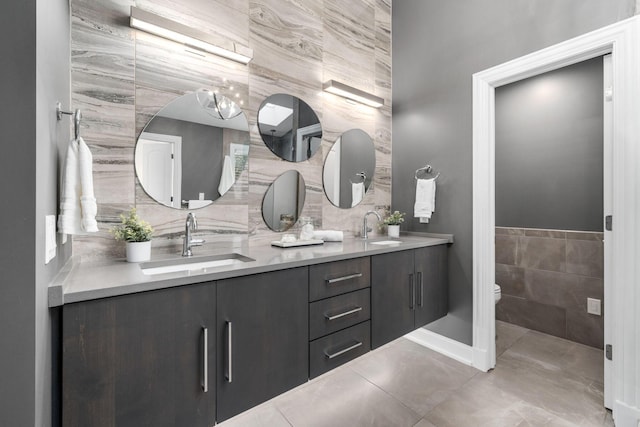 full bath with a sink, tile walls, double vanity, and toilet
