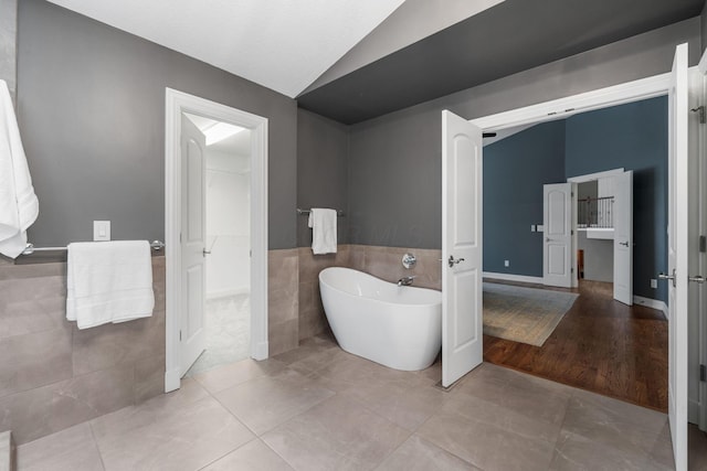 bathroom featuring a freestanding tub, tile walls, vaulted ceiling, a wainscoted wall, and tile patterned flooring
