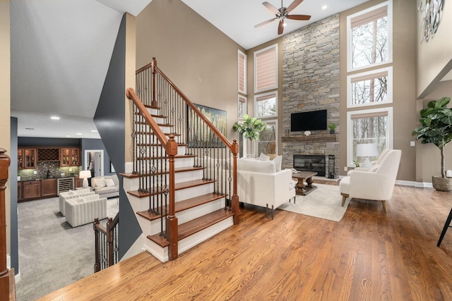 interior space with baseboards, a stone fireplace, a high ceiling, a ceiling fan, and wood finished floors