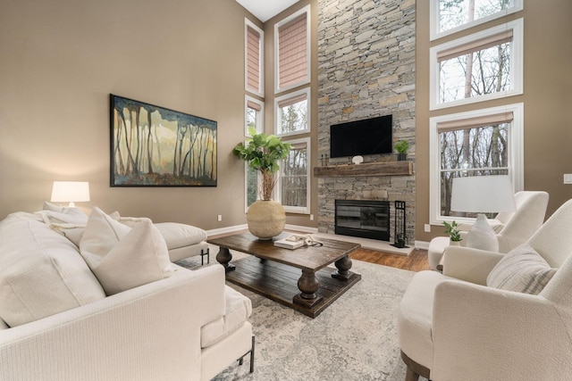 living room featuring baseboards, a towering ceiling, wood finished floors, and a fireplace