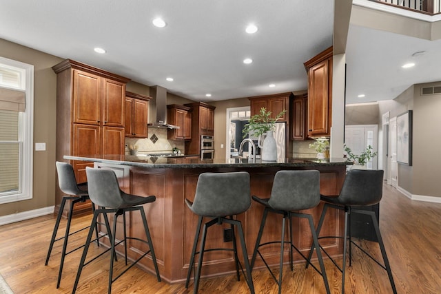 kitchen featuring a peninsula, light wood-type flooring, wall chimney range hood, visible vents, and stainless steel appliances
