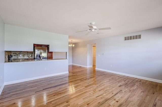 unfurnished living room with visible vents, baseboards, a sink, light wood finished floors, and ceiling fan with notable chandelier