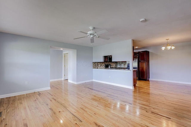 unfurnished living room with light wood-type flooring, baseboards, and ceiling fan with notable chandelier