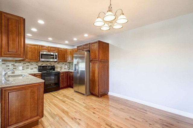 kitchen with decorative backsplash, appliances with stainless steel finishes, light wood-type flooring, a sink, and an inviting chandelier