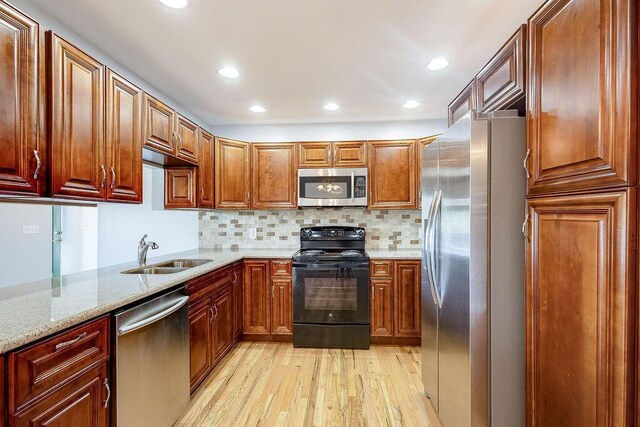 kitchen with appliances with stainless steel finishes, light wood-type flooring, a sink, light stone counters, and recessed lighting