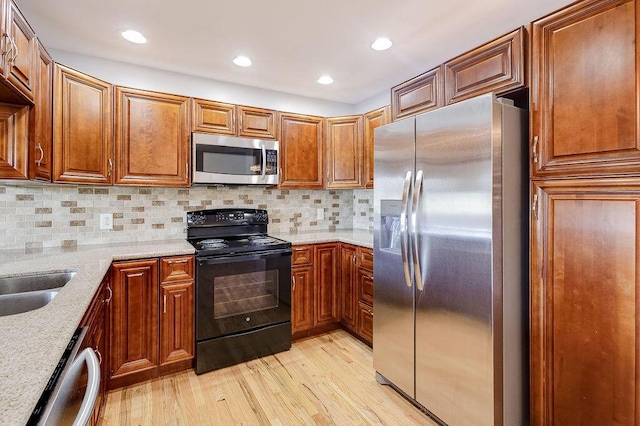 kitchen featuring brown cabinetry, light stone countertops, light wood-style floors, tasteful backsplash, and appliances with stainless steel finishes