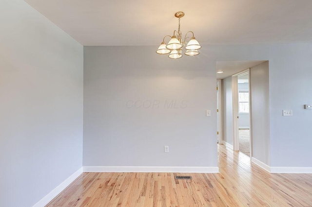 empty room with visible vents, light wood-style flooring, baseboards, and an inviting chandelier