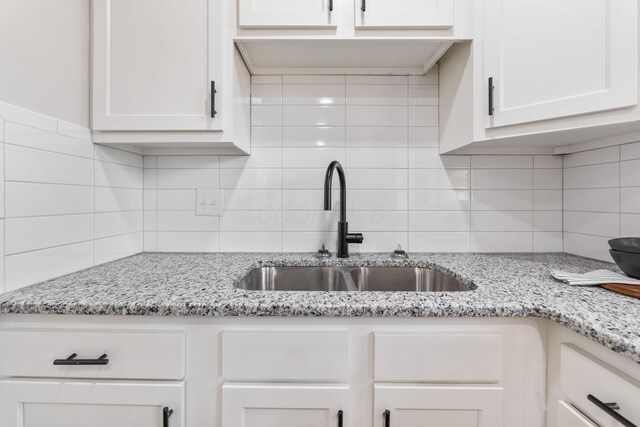 kitchen with white cabinetry, a sink, light stone counters, and decorative backsplash