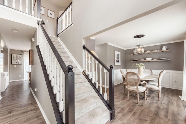 staircase with ornamental molding, wood finished floors, a decorative wall, and wainscoting