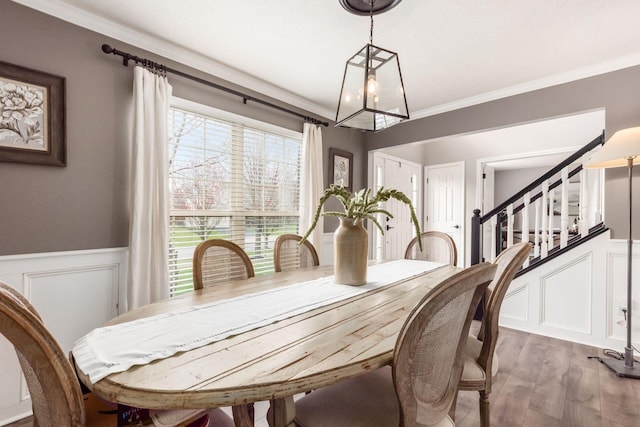 dining area with a decorative wall, ornamental molding, wood finished floors, an inviting chandelier, and wainscoting