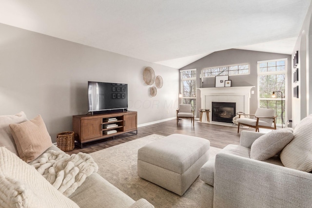 living area featuring baseboards, vaulted ceiling, a tiled fireplace, and wood finished floors