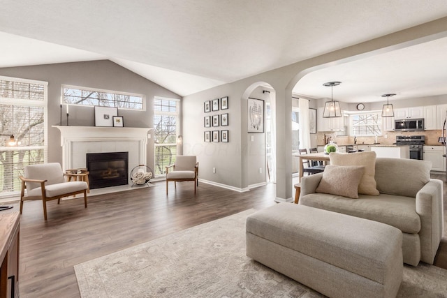 living area with lofted ceiling, baseboards, arched walkways, a tile fireplace, and wood finished floors