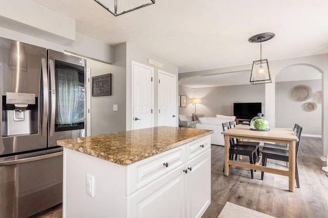 kitchen with arched walkways, white cabinetry, stone counters, light wood-type flooring, and stainless steel fridge with ice dispenser