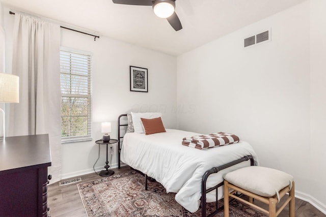 bedroom with a ceiling fan, wood finished floors, baseboards, and visible vents