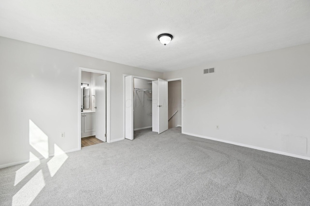 unfurnished bedroom with light colored carpet, ensuite bathroom, baseboards, visible vents, and a closet