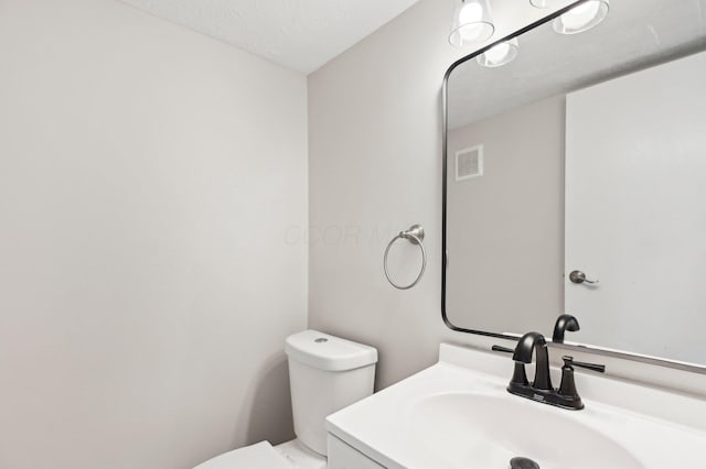half bath featuring visible vents, toilet, and vanity