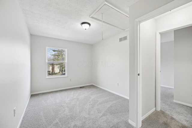 unfurnished room featuring carpet, a textured ceiling, visible vents, and attic access