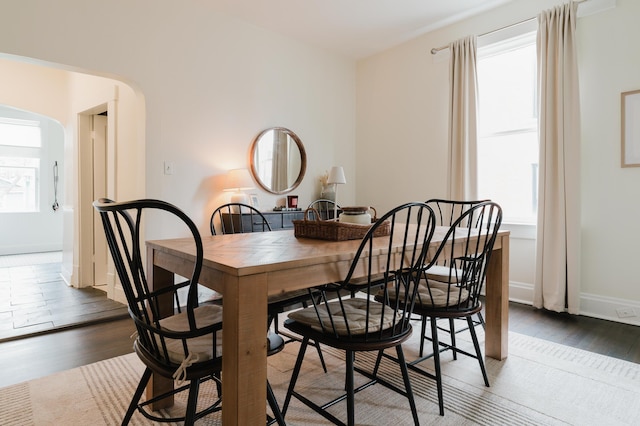 dining area with arched walkways, baseboards, and wood finished floors