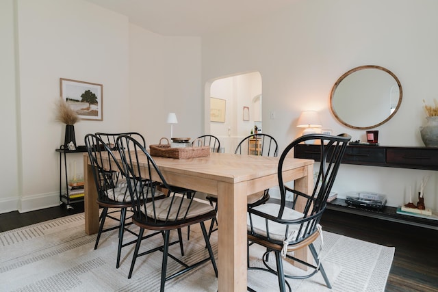 dining space with baseboards, arched walkways, and wood finished floors