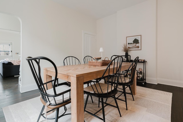 dining space featuring arched walkways, wood finished floors, and baseboards