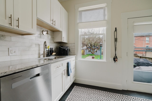 kitchen with light stone counters, a wainscoted wall, white cabinets, stainless steel dishwasher, and a sink