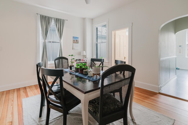 dining space featuring arched walkways, light wood-style floors, and baseboards