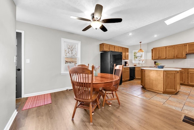dining space with vaulted ceiling, light wood-type flooring, baseboards, ceiling fan, and visible vents
