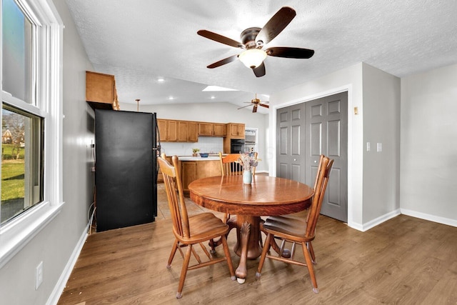 dining space with lofted ceiling, a textured ceiling, light wood-style flooring, and a ceiling fan