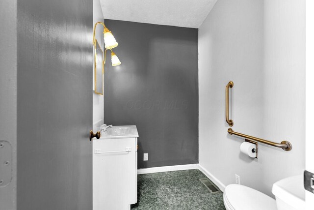 half bath featuring vanity, toilet, baseboards, a textured ceiling, and visible vents