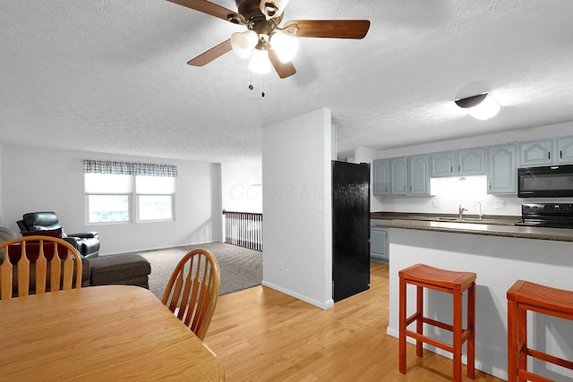 572 Sycamore Dr, Pickerington, OH 43147 - kitchen featuring black appliances, open floor plan, a textured ceiling, dark countertops, and light wood finished floors