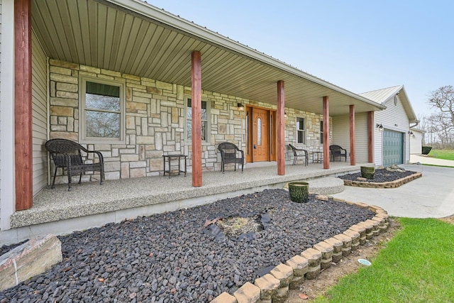 exterior space featuring concrete driveway, stone siding, an attached garage, and covered porch