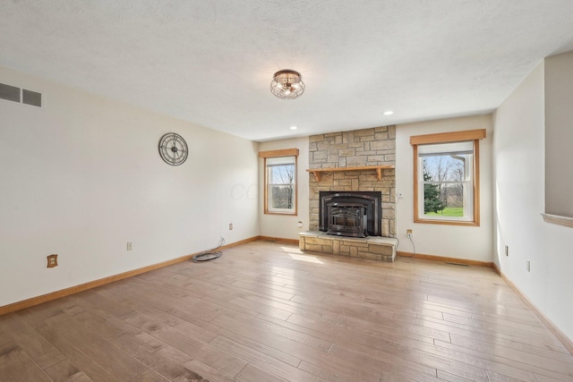 unfurnished living room with light wood finished floors, visible vents, baseboards, and a textured ceiling