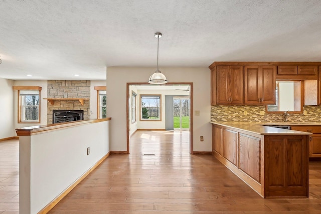 kitchen with tasteful backsplash, a peninsula, light wood-style flooring, light countertops, and brown cabinetry