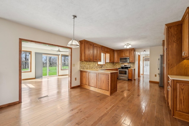 kitchen with brown cabinets, decorative backsplash, a peninsula, and stainless steel appliances