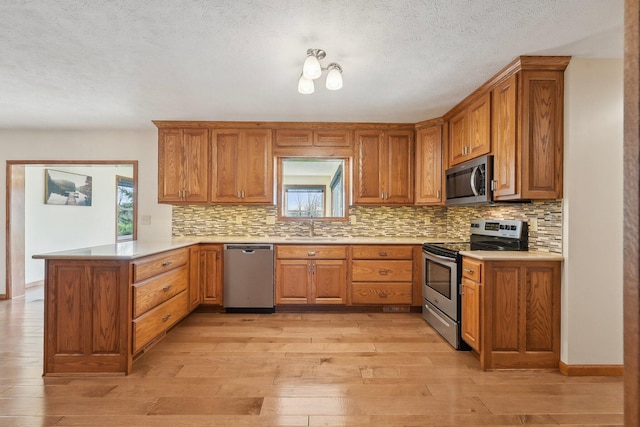 kitchen featuring a wealth of natural light, brown cabinetry, a peninsula, a sink, and stainless steel appliances