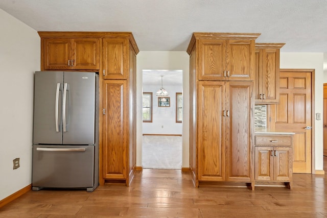 kitchen with freestanding refrigerator, light wood-style flooring, brown cabinetry, light countertops, and baseboards
