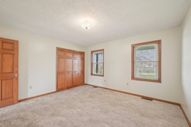 unfurnished bedroom with light colored carpet, visible vents, a closet, and baseboards